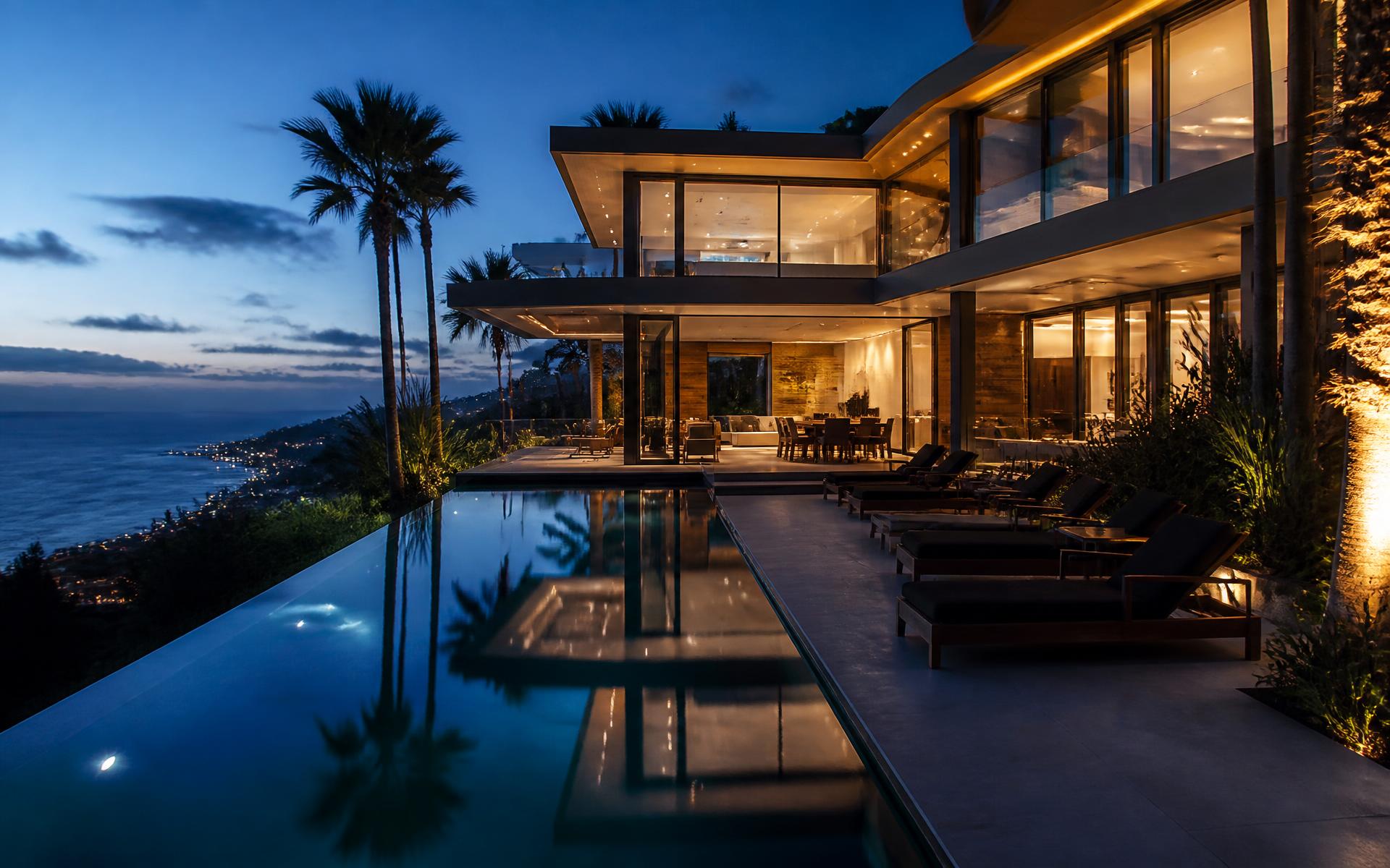 Modern luxury hillside home at twilight with infinity pool and ocean view
